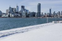 a person riding a bicycle on a snowy street near a city skyline with the ocean in front