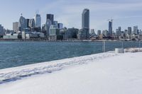 a person riding a bicycle on a snowy street near a city skyline with the ocean in front