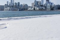 a person riding a bicycle on a snowy street near a city skyline with the ocean in front