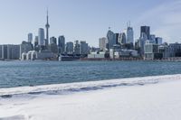 a person riding a bicycle on a snowy street near a city skyline with the ocean in front