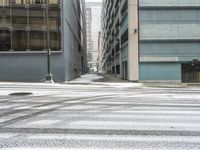 a street corner is snowy covered in snow and empty parking spaces in the background is a tall building with windows