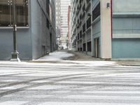 a street corner is snowy covered in snow and empty parking spaces in the background is a tall building with windows