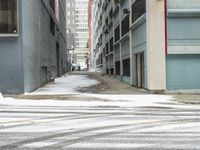 a street corner is snowy covered in snow and empty parking spaces in the background is a tall building with windows