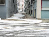 a street corner is snowy covered in snow and empty parking spaces in the background is a tall building with windows