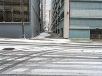 a street corner is snowy covered in snow and empty parking spaces in the background is a tall building with windows