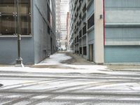 a street corner is snowy covered in snow and empty parking spaces in the background is a tall building with windows