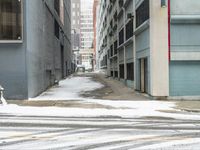 a street corner is snowy covered in snow and empty parking spaces in the background is a tall building with windows