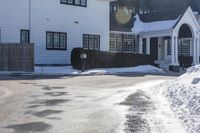 the white home is located on a snow - filled suburban street with a fence that has a few snow piles