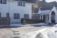 the white home is located on a snow - filled suburban street with a fence that has a few snow piles