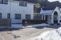 the white home is located on a snow - filled suburban street with a fence that has a few snow piles