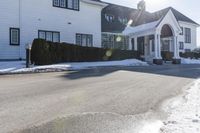 the white home is located on a snow - filled suburban street with a fence that has a few snow piles