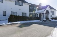 the white home is located on a snow - filled suburban street with a fence that has a few snow piles