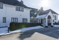 the white home is located on a snow - filled suburban street with a fence that has a few snow piles