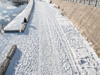 a person standing in the snow on the edge of a walkway at a lake bank