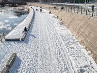 a person standing in the snow on the edge of a walkway at a lake bank