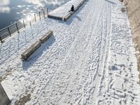 a person standing in the snow on the edge of a walkway at a lake bank