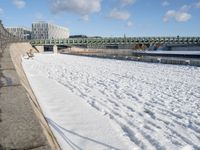 this is a snowy area where there is snow on the ground and benches are near the water