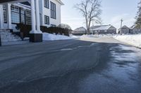 the white house has snow piled on its sidewalk and front door, two front porchs with columns