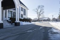 the white house has snow piled on its sidewalk and front door, two front porchs with columns