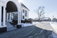 the white house has snow piled on its sidewalk and front door, two front porchs with columns