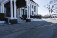 the white house has snow piled on its sidewalk and front door, two front porchs with columns