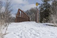 a snow covered field that has tracks on it and a wooden bridge over the water