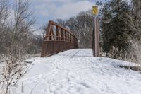 a snow covered field that has tracks on it and a wooden bridge over the water