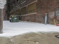 a group of garbage can sitting by some snow covered sidewalk and brick building in a wintery area