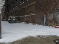 a group of garbage can sitting by some snow covered sidewalk and brick building in a wintery area