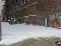 a group of garbage can sitting by some snow covered sidewalk and brick building in a wintery area