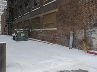 a group of garbage can sitting by some snow covered sidewalk and brick building in a wintery area