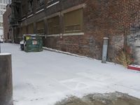 a group of garbage can sitting by some snow covered sidewalk and brick building in a wintery area