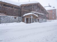 a tall brown wooden house with several windows in the snow near a road with a person walking up the sidewalk next to it