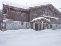 a tall brown wooden house with several windows in the snow near a road with a person walking up the sidewalk next to it