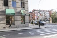 people crossing the street in front of a building with a crosswalk and two cars