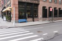 there is a bench near the street corner by a brick building where you can eat and stay