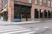 there is a bench near the street corner by a brick building where you can eat and stay