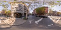 an image of a 360 lens of people riding bikes on the street corner and a red brick building to the left