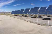 solar panels are seen on a dirt lot, while clouds float in the sky above