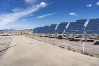 solar panels are seen on a dirt lot, while clouds float in the sky above