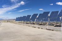 solar panels are seen on a dirt lot, while clouds float in the sky above