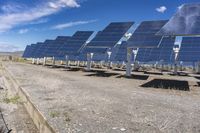 a row of large solar panels near some grass and dirts with blue sky in the background