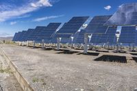 a row of large solar panels near some grass and dirts with blue sky in the background