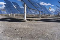 rows of solar panels are in a field on the ground with blue skies in the background