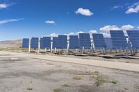 a row of solar panels in the foreground under a blue sky with clouds and green grass