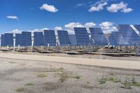 a row of solar panels in the foreground under a blue sky with clouds and green grass