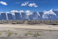 a row of solar panels in the foreground under a blue sky with clouds and green grass