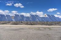 rows of solar panels sit on a paved area against a blue sky with white clouds