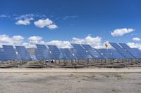 rows of solar panels sit on a paved area against a blue sky with white clouds