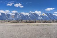 rows of solar panels sit on a paved area against a blue sky with white clouds